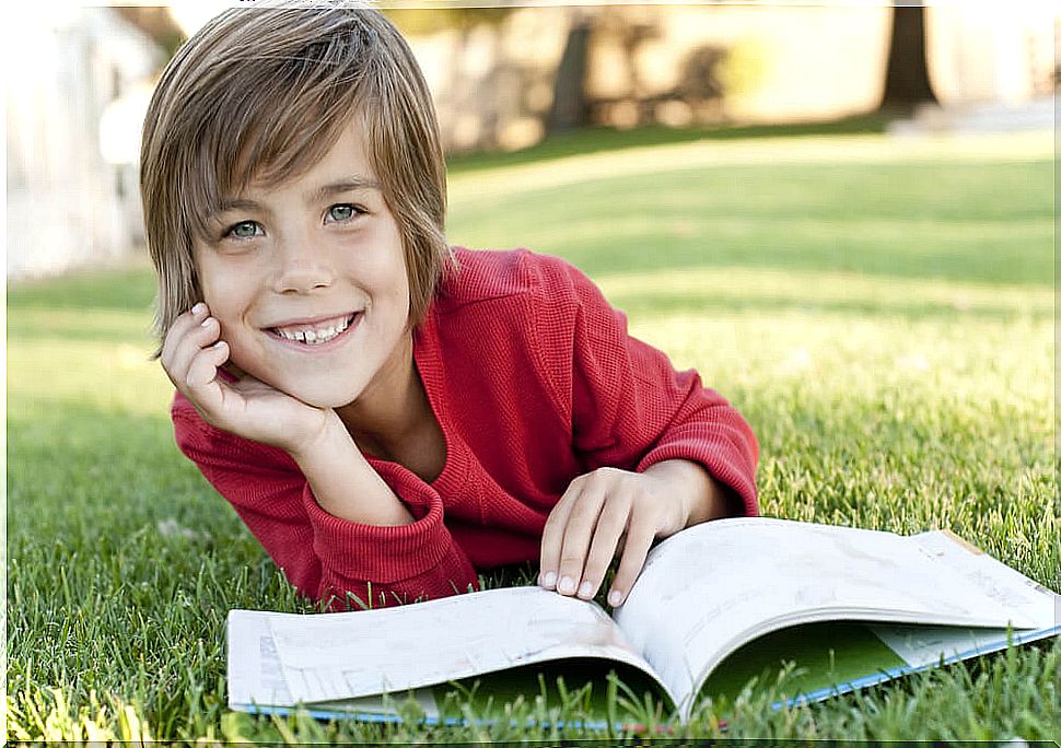 Boy reading a book lying on the grass.