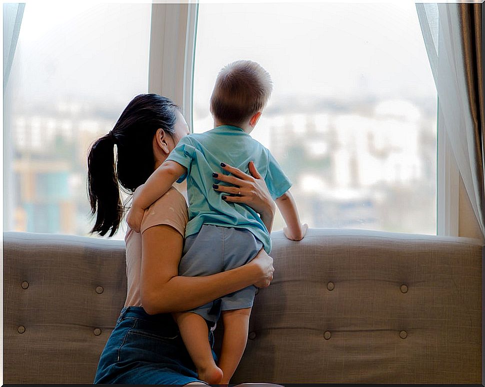 Mother and son looking out the window spending free time together during confinement.