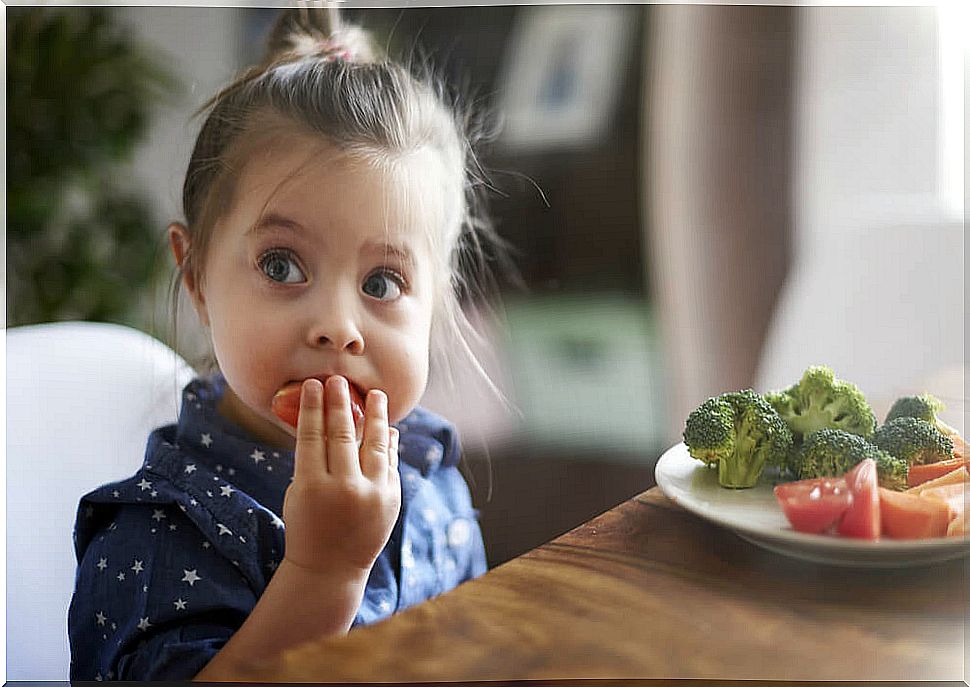 Little girl eating fruits and vegetables at the table because she has good eating habits.