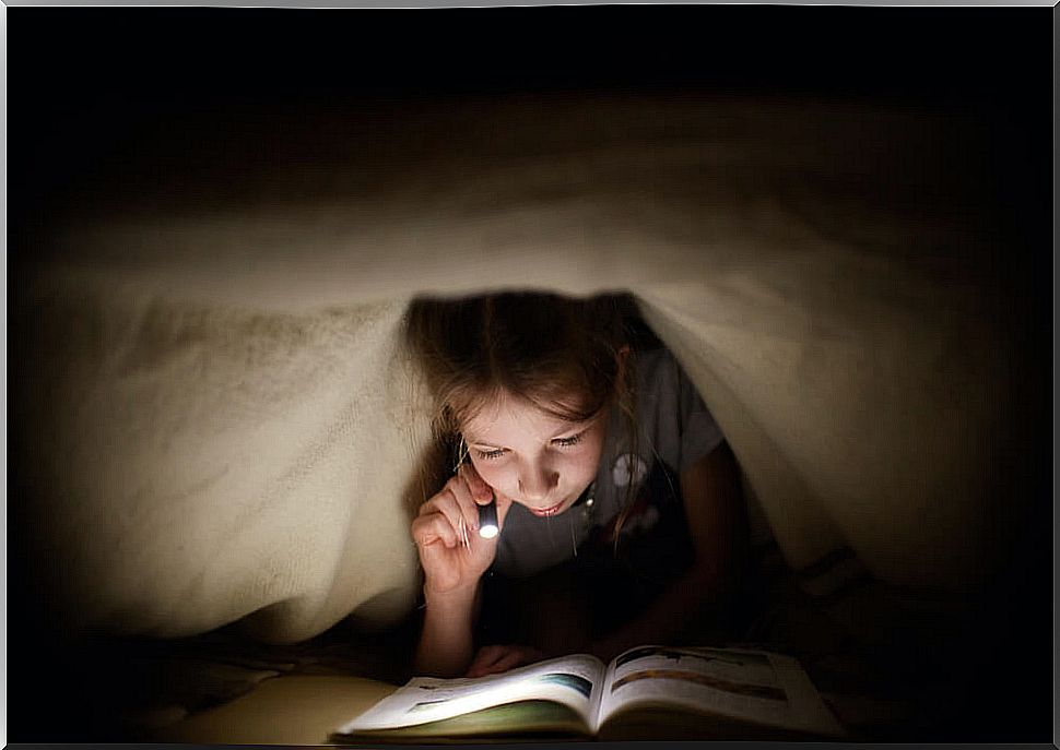 Child reading modern children's stories under the duvet with a flashlight.